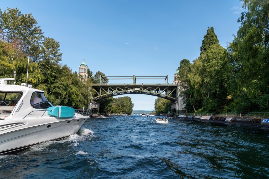 Un bateau à moteur navigue sur un canal encadré de verdure, passant sous un pont ancien, illustrant les conditions d’un permis fluvial