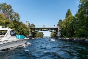Un bateau à moteur navigue sur un canal encadré de verdure, passant sous un pont ancien, illustrant les conditions d’un permis fluvial