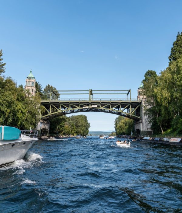Navigation fluviale sous un pont – Apprentissage permis bateau Un bateau à moteur navigue sur un canal encadré de verdure, passant sous un pont ancien, illustrant les conditions d’un permis fluvial